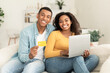 © Prostock-studio - Cheerful young african american family use credit card, laptop and banking, check financial account, sit on sofa