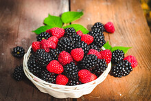 Blackberry And Raspberry In A White Basket Under Sunlight On A Wooden Background