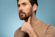 © Prostock-studio - Portrait of handsome caucasian bearded man examining his face, touching beard while posing over blue background