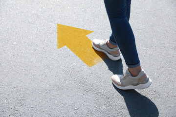 Planning future. Woman walking to drawn mark on road, closeup. Yellow arrow showing direction of way