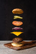 © Cavan Images - Separated burger with floating ingredients on black background.