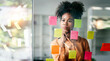 Leinwanddruck Bild - Young smiley attractive, businesswoman using sticky notes in glass wall to writing strategy business plan to development grow to success