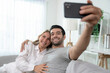 © Basicdog - Caucasian couple video calling talking with friends on mobile phone in living room.