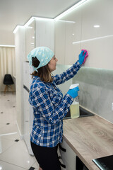 Wall Mural - woman in a headscarf and gloves in the kitchen washes the kitchen set and the hood with cloth.