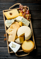 Different types of cheese in a wooden tray with grapes .