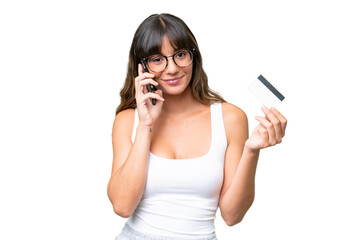 Wall Mural - Young caucasian woman over isolated background keeping a conversation with the mobile phone and holding a credit card