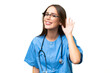 Young nurse caucasian woman over isolated background listening to something by putting hand on the ear