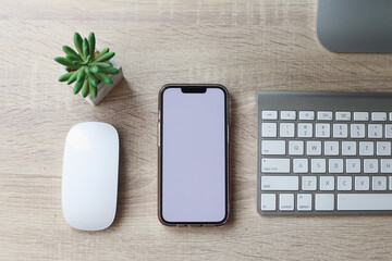 Top view of minimal workspace with blank screen smartphone, keyboard laptop on wooden office desk