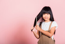 Asian Little Kid 10 Years Old Hold Comb Brushing Her Unruly She Touching Her Long Black Hair At Studio Shot Isolated On Pink Background, Happy Child Girl With A Hairbrush, Hair Care Concept