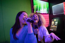 Happy Young Friends Singing Karaoke In Microphone At Amusement Arcade
