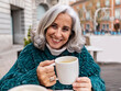 © Westend61 - Happy senior woman with coffee cup sitting in sidewalk cafe