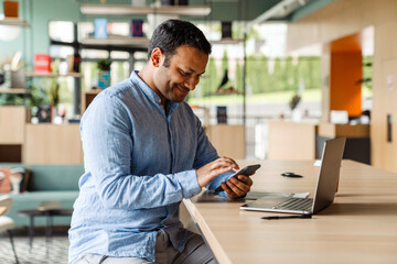 Wall Mural - Young businessman in formal wear using laptop and cellphone at office