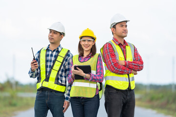 Wall Mural - Photo of a team of 3 engineers or architects, male and female, smiling, smart, wearing uniforms and helmets. Stand together in strength and unity. ready to work on industrial structures.