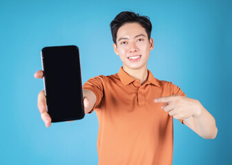 Wall Mural - Image of young Asian man holding smartphone on blue background