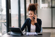 © Nuttapong punna - Business Africa woman Talking on the phone and using a laptop with a smile while sitting at modern office