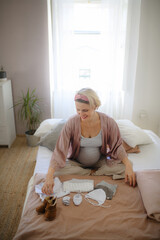 Wall Mural - High angle view of pregnant woman looking at little clothes for her baby, packing them to maternity ward.