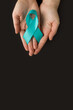 Hands holding Teal ribbon on black background, Symbolic for cervical cancer, ovarian cancer, gynecological cancer and PCOS. And sexual assault awareness. Women's health care