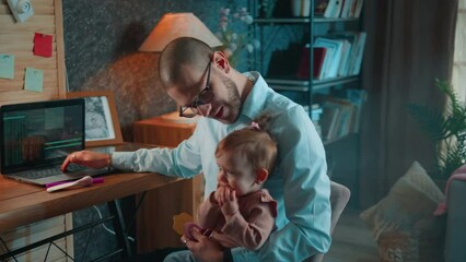 Application developer is working on his laptop and taking care of his baby daughter