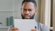 Unhappy African American bearded guy man received bad news reading letter with bank refuse feeling stressed about dismissal notice. Angry sad ethnic businessman read credit loan refusal notification