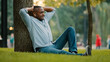 © Yuliia - Happy calm relaxed elderly middle-aged mature senior adult African American ethnic man in wireless headphones sitting on grass in city park under tree listen music audio song in smartphone outdoors