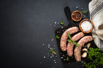 Wall Mural - Bratwurst or sausages on cutting board with rosemary at black table. Ready for cooking. Top view with copy space.