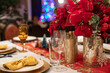 Table de fête avec couverts et verres de luxe, serviettes, assiettes et vases dorés, nappe blanche et napperon brodé rouge. Décoration et étoiles de Noël rouges.