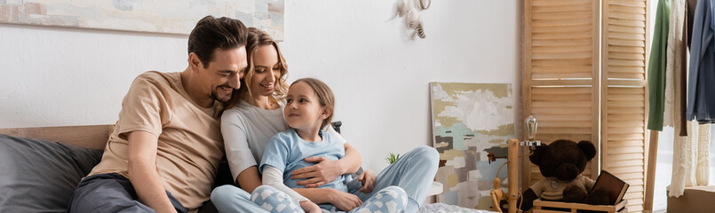 happy woman hugging daughter near husband while resting on bed, banner.