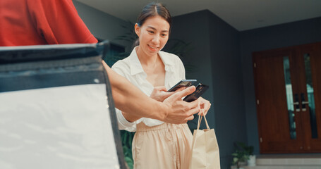 Wall Mural - Young happy Asian woman accept paper bag from delivery man with bicycle in red uniform carry case box scan QR code payment on smartphone in front of house. express food delivery concept.