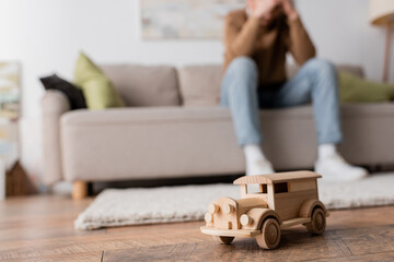 Wall Mural - wooden toy vehicle near cropped blurred man sitting on couch in living room.