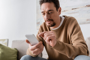 Wall Mural - bearded man in beige jumper using smartphone at home.