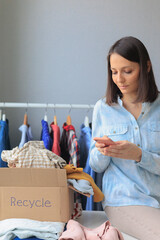 Wall Mural - recycling, woman collects clothes for donation writes to secondhand service online, sort out textiles, paper home, hand over to garbage disposal service. cardboard box with colored shirts, sweaters