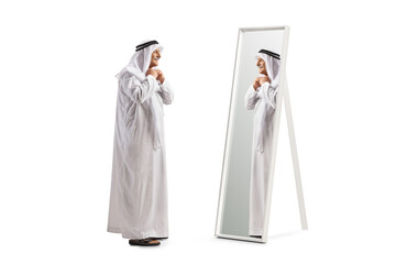 Wall Mural - Full length profile shot of a mature arab man in a white robe standing in front of a mirror