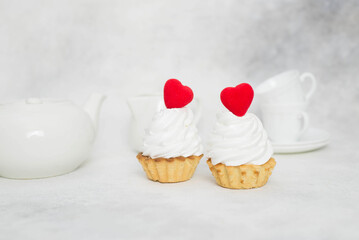 two cakes with red hearts and teapot, cups on a gray background.