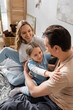 © LIGHTFIELD STUDIOS - cheerful kid looking at father near happy mother smiling while sitting on bed.