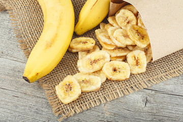 Poster - Healthy food - slices of dried banana and fresh bananas on a wooden background. Banana crispy chips.