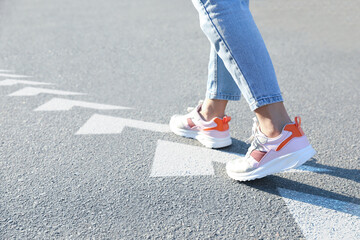 Wall Mural - Planning future. Woman walking on drawn marks on road, closeup. White arrows showing direction of way