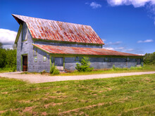 Bright Blue Sky Set Behind Gray Old Barn With Rusted Roof In Kingfield, Maine.