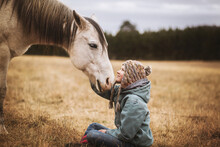 Young Girl Sitting While Touching Horse Head