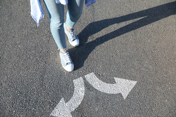 Wall Mural - Choice of way. Woman walking towards drawn marks on road, closeup. White arrows pointing in opposite directions