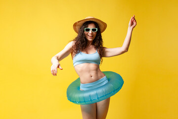 Wall Mural - young curly brunette girl in a blue swimsuit in summer with an inflatable swimming ring dances and moves