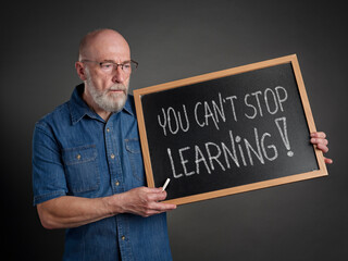 Sticker - you can not stop learning, white chalk writing on a blackboard held by a senior man, teacher, mentor or presenter, education, lifestyle and personal development concept