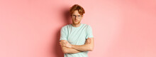 Angry Man In Glasses With Red Hair Frowning, Cross Arms On Chest In Defensive Pose, Sulking At You, Standing Over Pink Background