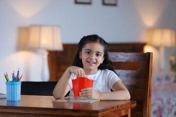 little happy girl eating french fries and enjoying the food at home - childhood study room . smiling