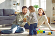 Cute little girl playing game with her parents at home. Smiling dad giving golden Christmas ball to his toddler daughter, mom looking at her with tenderness. Happy family playing toys together