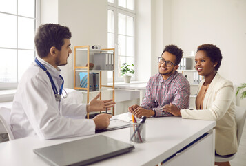 Wall Mural - Male gynecologist talk consult multiethnic couple at meeting in private clinic. Smiling man doctor speak with multiracial patients at consultation in hospital. Good medicine, healthcare concept.