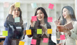 © David - Young creative business Asian woman standing with her colleagues writing new ideas on sticky notes over glass wall, business marketing strategy or User experience ux ui concept.