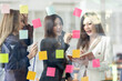 © David - Young creative business Asian woman standing with her colleagues writing new ideas on sticky notes over glass wall, business marketing strategy or User experience ux ui concept.