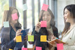 © David - Young creative business Asian woman standing with her colleagues writing new ideas on sticky notes over glass wall, business marketing strategy or User experience ux ui concept.