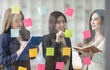 © David - Young creative business Asian woman standing with her colleagues writing new ideas on sticky notes over glass wall, business marketing strategy or User experience ux ui concept.