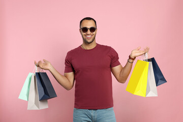 Wall Mural - Happy African American man in sunglasses with shopping bags on pink background